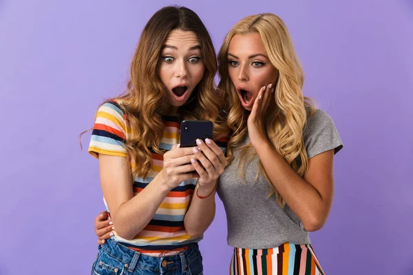 かなり陽気な若い女の子友達を つ紫色の背景に分離立って携帯を見て — ストック写真