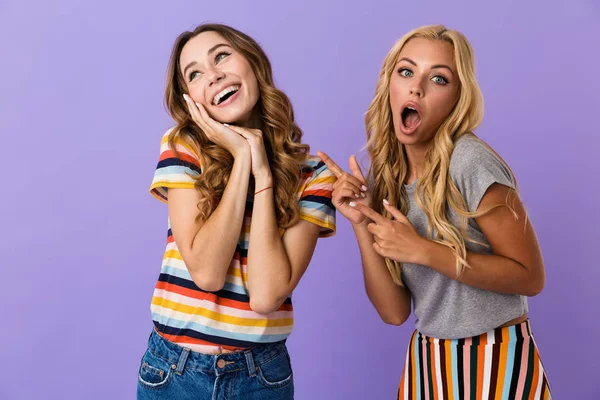 Дві Красиві Молоді Дівчата Друзі Стоять Ізольовані Фіолетовому Фоні Вказуючи — стокове фото