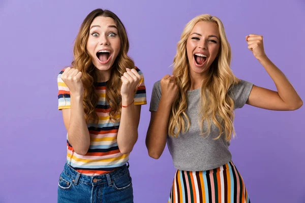 两个漂亮的年轻女孩的朋友站在紫色背景隔绝 庆祝成功 — 图库照片