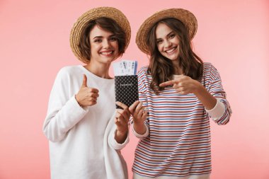 Bilet ve pasaport elinde pembe bir arka plan üzerinde izole poz heyecanlı mutlu sevimli genç kadın arkadaşlar görüntü.