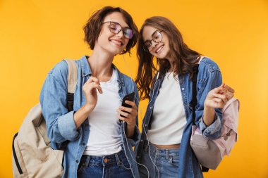 Hareket eden telefon dinleme müzik kulaklık kullanarak sarı duvar arka plan üzerinde neşeli mutlu kadın arkadaşlar görüntü izole.