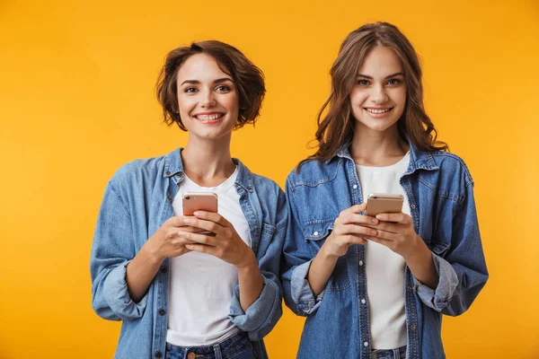 Mutlu Genç Kadın Arkadaşlar Cep Telefonunu Kullanarak Sarı Duvar Arka — Stok fotoğraf