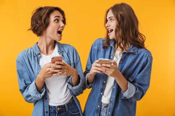 興奮して若い女性の友人が携帯電話を使った黄色の壁の背景に分離の感情的なイメージ — ストック写真