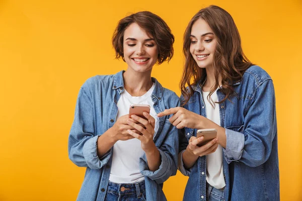 携帯電話を使った黄色の背景に分離されたポーズの陽気な幸せ感情的な若い女性の友人の写真 — ストック写真