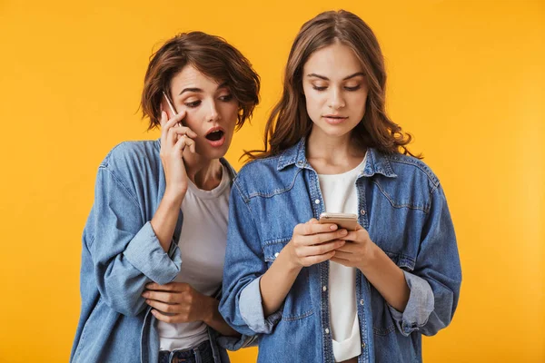 歓談の携帯電話を使用して黄色の壁の背景に分離された感情的な若い女性の友人のイメージ — ストック写真