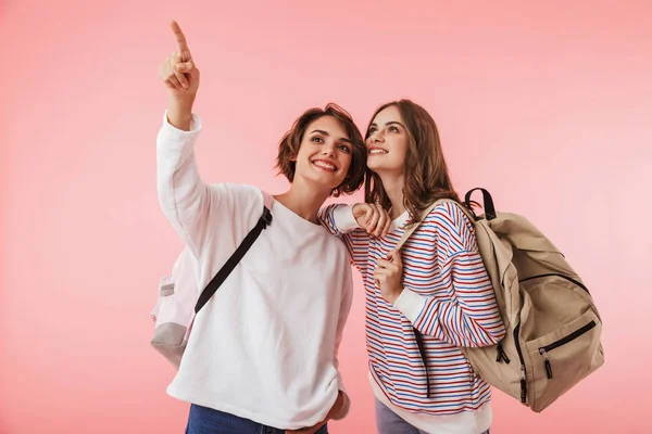 幸せな女性の友人のイメージが指しているバックパックを保持しているピンクの壁の背景の上分離 — ストック写真