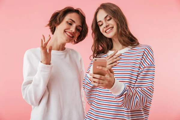 携帯電話を使用してピンクの壁の背景に分離された幸せな女性友人のイメージ — ストック写真