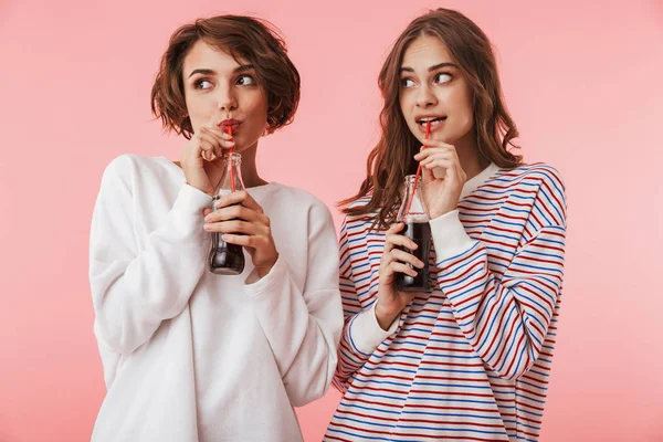 Görüntüsünü neşeli kadın arkadaşlar soda içme pembe duvar arka plan üzerinde izole mutlu.