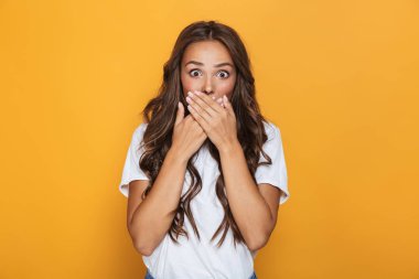 Sarı arka plan üzerinde izole ellerle ağız kapsayan uzun saçlı sürpriz kadın 20'li yaşlarda görüntüsünü