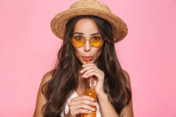 照片特写的迷人的女人20S 戴墨镜和草帽喝果汁从玻璃瓶查出粉红色背景 — 图库照片