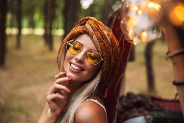 Orman kampında istirahat ederken gülümseyen şık güneş gözlüğü takıyor sarışın sevimli kadın fotoğrafı