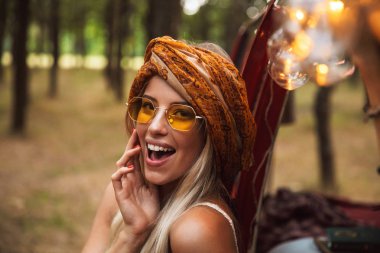 Şık aksesuarlar orman kampında istirahat ederken gülümseyen giymiş sarışın hippi kadın fotoğrafı