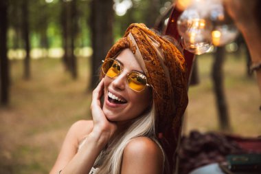 Vintage aksesuarları orman kampında istirahat ederken gülümseyen giymiş sarışın sevimli kadın görüntüsünü