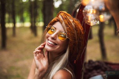 Şık aksesuarlar orman kampında istirahat ederken gülümseyen giyen neşeli sevimli kadın fotoğrafı