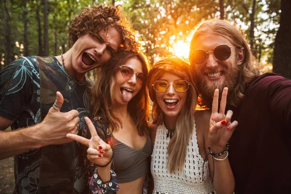 Photo of joyful hippie people men and women smiling and taking selfie in forest