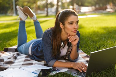 Görüntü şaşırtıcı ciddi kadın öğrenci açık havada dizüstü bilgisayar kullanan bir parkta yatıyor.