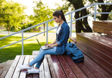 Açık havada dizüstü bilgisayar kullanan oturan şaşırtıcı genç güzel kadın görüntüsünü.