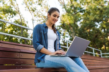 Açık havada dizüstü bilgisayar kullanan oturan şaşırtıcı genç güzel kadın görüntüsünü.