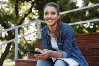 Görüntü oldukça mutlu neşeli Genç beyaz kadının açık havada cep telefonuyla sohbet oturan.