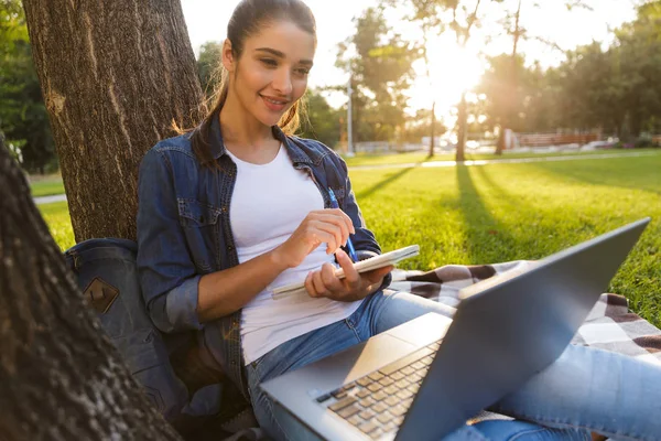 ノート書きにラップトップ コンピューターを使用して公園内の素晴らしい美しい若い女性学生のイメージ — ストック写真