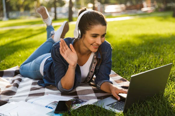 惊人的快乐的妇女学生的形象躺在户外在公园使用笔记本电脑听音乐挥舞 — 图库照片