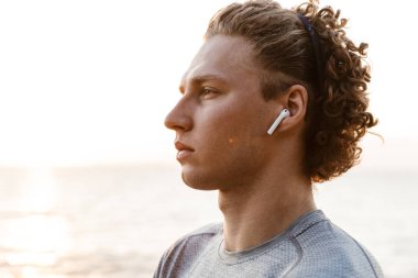 Görüntü yakışıklı genç adam plaj kulaklık ile müzik dinleme üzerinde ayakta spor.