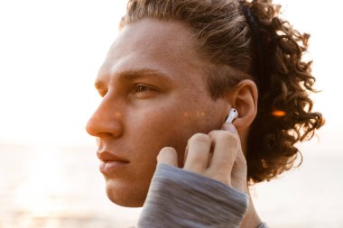 Görüntü yakışıklı genç adam plaj kulaklık ile müzik dinleme üzerinde ayakta spor.