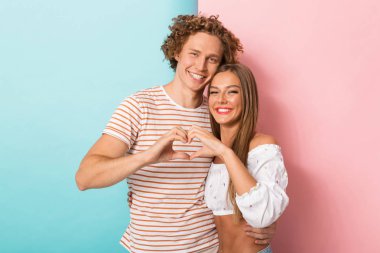 İki renkli arka plan üzerinde duran, kalp jest yapmak mutlu bir genç çift portresi