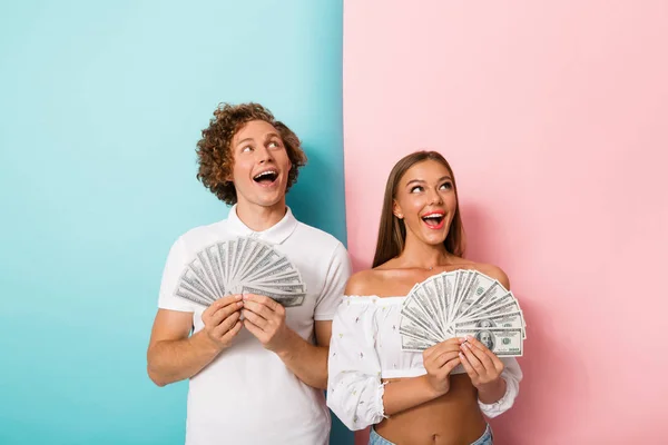 一个欢快的年轻夫妇的肖像站在两个彩色背景 显示钞票 — 图库照片