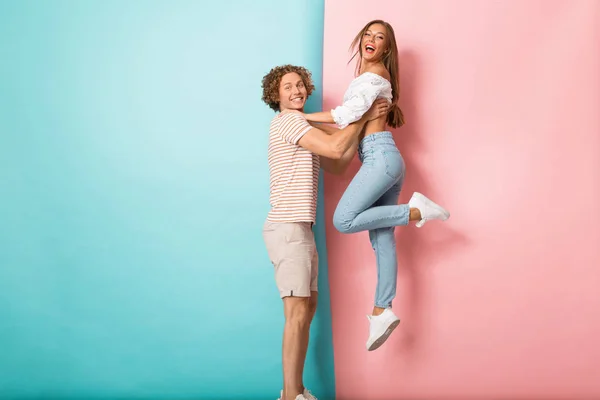 彼のガール フレンドを持ち上げる男 つの色付きの背景上に立って幸せな若いカップルの完全な長さの肖像画 — ストック写真