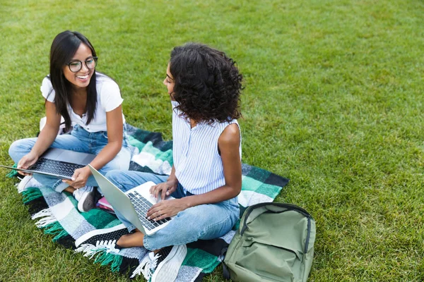 Dwa Uśmiechnięte Młode Dziewczyny Studentów Siedzi Trawie Kampusie Studia Komputerów — Zdjęcie stockowe