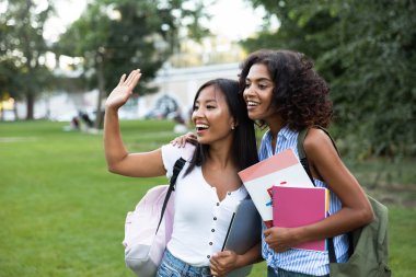 İki genç kız öğrencilerine açık havada ayakta sallayarak gülümseyen