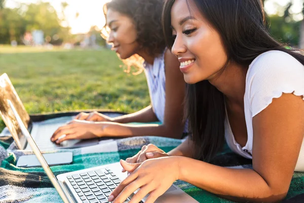 关闭两个漂亮的女孩学生在校园里躺在草地上 用笔记本电脑学习 — 图库照片