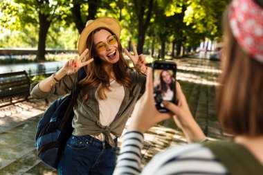 Cep telefonu tarafından barış hareketi gösterilen bir fotoğraf almak mutlu hanımlar arkadaşlar açık havada yürüyüş sırt çantaları ile fotoğraf.