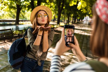 Öpücük üfleme cep telefonuyla bir fotoğraf almak mutlu hanımlar arkadaşlar açık havada yürüyüş sırt çantaları ile fotoğraf.