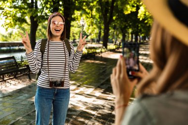 Cep telefonu tarafından barış hareketi gösterilen bir fotoğraf almak mutlu hanımlar arkadaşlar açık havada yürüyüş sırt çantaları ile fotoğraf.