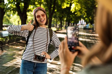 Fotoğraf genç mutlu bayanlar arkadaşlar açık havada yürümek ile bir fotoğraf tarafından cep telefonu başparmak makyaj almak sırt çantaları.