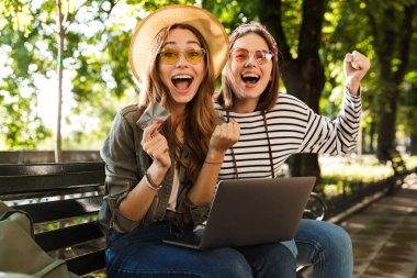 Mutlu bayanlar arkadaşlar açık havada oturma kredi kartı dizüstü bilgisayarı kullanarak fotoğraf genç duygusal heyecanlı.