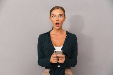 Cep telefonu kullaranarak gri duvar arka plan üzerinde izole görüntü şok iş genç kadının poz.
