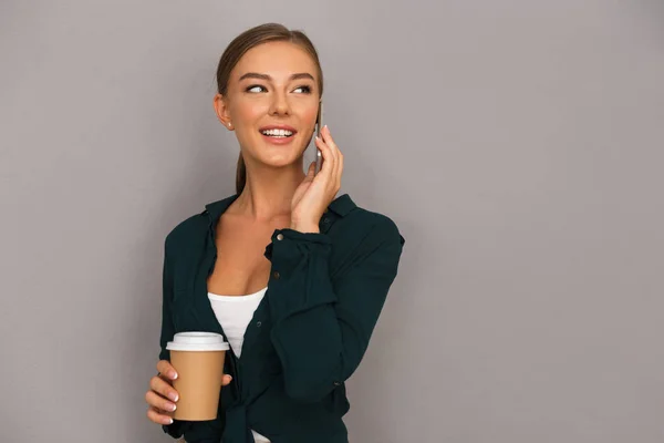 Image of excited beautiful business woman posing isolated over grey wall background drinking coffee talking by mobile phone.