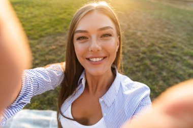 Gülümseyen genç bir kadın uzanmış eller ile parkta bir selfie alarak yakın çekim