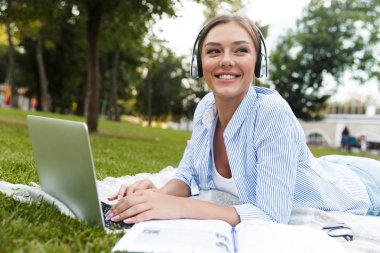 Görüntü güzel genç güzel kadın Park açık havada kullanarak dizüstü bilgisayar müzik dinleme.