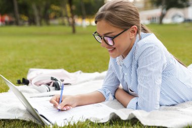 Güzel genç güzel kadın Park açık havada notlar yazma dizüstü bilgisayar kullanan görüntü.