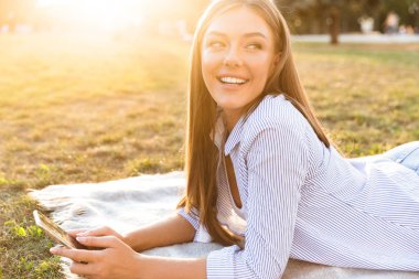 Bir battaniye yeşil park üzerinde döşeme ise genç kız holding cep telefonu gülümseyen