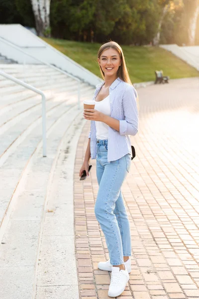 Sonriente Chica Joven Con Mochila Sosteniendo Café Para Llevar Mientras —  Fotos de Stock