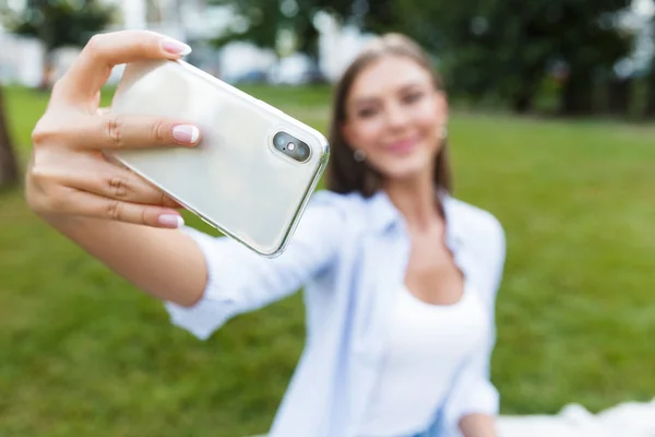 公園屋外で驚くほど若いきれいな女性のイメージは 携帯電話で Selfie を取る — ストック写真