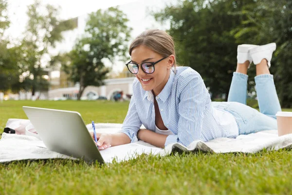 美丽的年轻漂亮的女人在公园户外使用笔记本电脑书写笔记的形象 — 图库照片