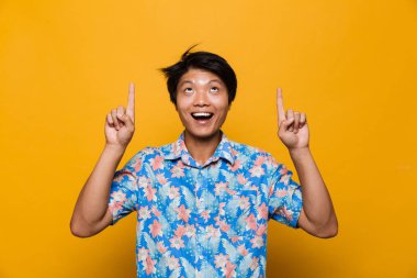 Heyecanlı bir genç Asyalı adamın poz görüntü sarı arka plan işaret içinde izole.