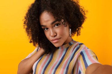 Görüntü güzel genç Afrika şirin kızın sarı arka plan üzerinde izole poz almak bir selfie.