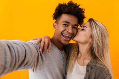 Kaç poz sevgi dolu mutlu sevimli genç görüntüsünü almak sarılma sarı arka plan üzerinde bir selfie kamera öperek izole.